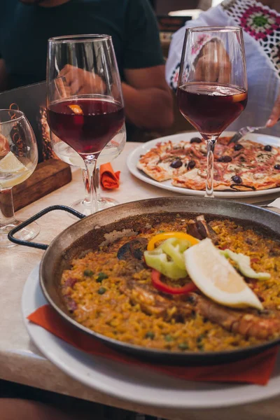 Geleneksel tavada tipik İspanyol deniz ürünleri paellası. Arka planda İspanyol sangriası olan bardaklar. Bir restoranda akşam yemeği..