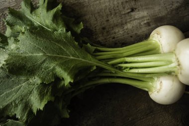 Hakiki ahşap zemin üzerinde taze yeşil kaplamalı ve kökleri olan rustik organik şalgam. Vejetaryen yemekleri, seçici odaklanma