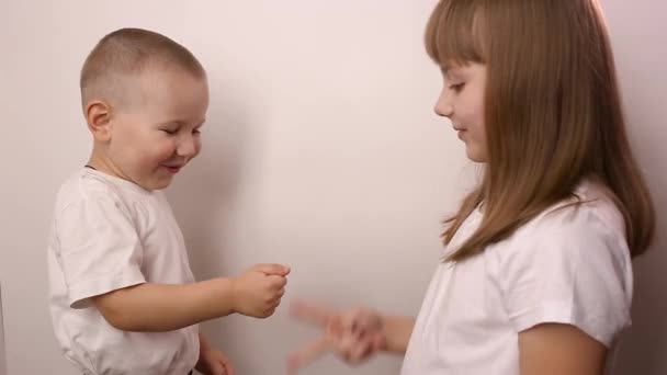 Счастливые дети играют в игру бумажные ножницы на белом фоне, улыбаются и смеются — стоковое видео