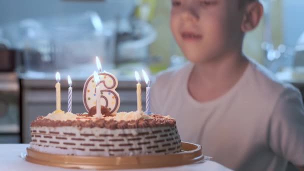 Niño sentado en la mesa de la cocina junto al pastel de cumpleaños con velas encendidas — Vídeos de Stock