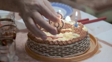 Erkek ellerine yakın plan. Doğum günü pastasının üzerinde mum ve kibrit yakıyorlar.