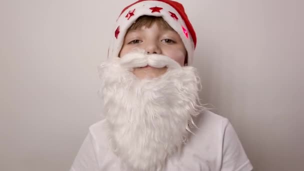 八岁的白人小女孩 戴着假胡子 戴着圣诞老人帽 闪烁着红灯 用白色背景拉着批准的大拇指 新年或圣诞节的服装庆祝活动 — 图库视频影像