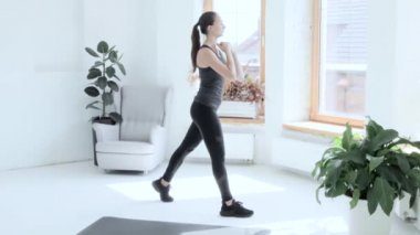 Spor giyimli esmer genç kız evde spor egzersizleri yapıyor. Çömeliyor.