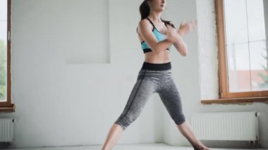 Spor kıyafetli genç esmer kız evdeki parlak odada egzersiz yapıyor.