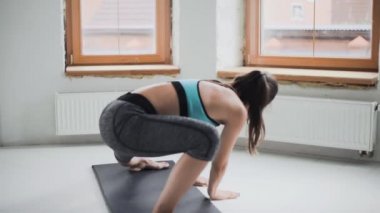 Spor kıyafetli genç esmer kız evdeki parlak odada egzersiz yapıyor.