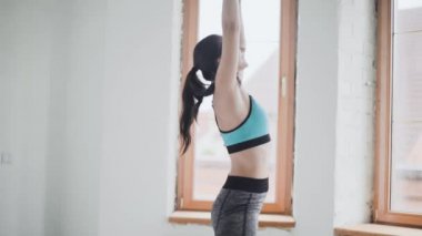 Spor kıyafetli genç esmer kız evdeki parlak odada egzersiz yapıyor.