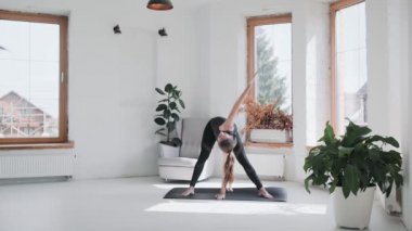 Spor kıyafetli genç esmer kız evdeki parlak odada egzersiz yapıyor.