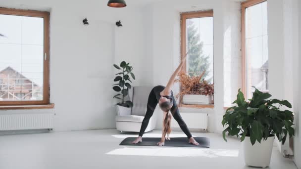 Jong sportief brunette meisje in sportkleding doet oefeningen in heldere kamer thuis — Stockvideo