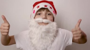 Noel Baba şapkalı yapay sakallı kız beyaz arka planda baş parmak kaldırıyor.