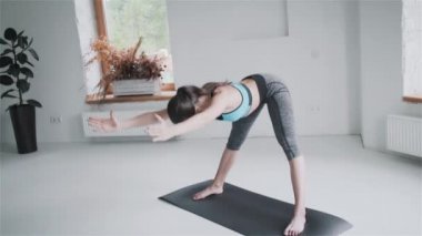 Spor kıyafetli genç esmer kız evdeki parlak odada egzersiz yapıyor.