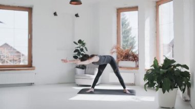 Spor kıyafetli genç esmer kız evdeki parlak odada egzersiz yapıyor.