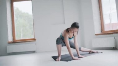 Spor kıyafetli genç esmer kız evdeki parlak odada egzersiz yapıyor.