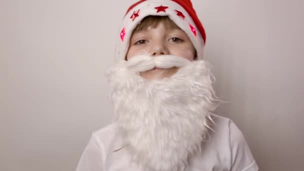Смешная маленькая девочка с искусственной бородой в шляпе Санта Клауса выпрямляет усы — стоковое видео