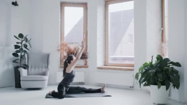 Spor kıyafetli genç esmer kız evdeki parlak odada egzersiz yapıyor.