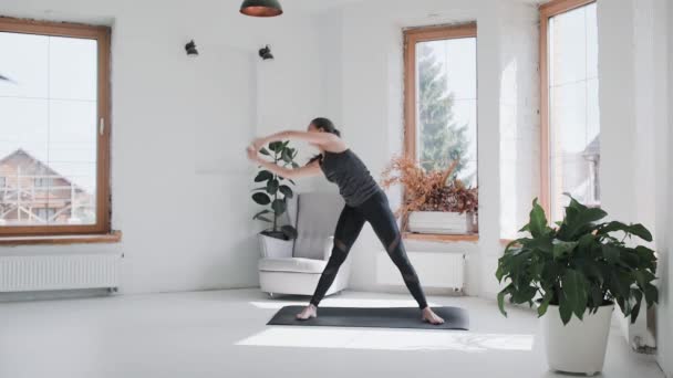 Joven chica morena deportiva en ropa deportiva hace ejercicios en habitación luminosa en casa — Vídeos de Stock