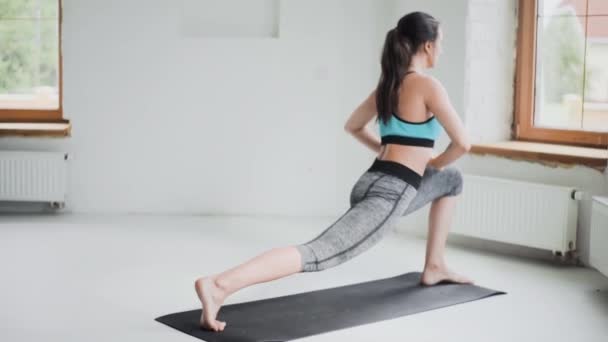 Jovem menina morena desportiva em sportswear faz exercícios no quarto brilhante em casa — Vídeo de Stock