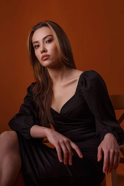 Elegant model wearing black dress with deep neckline posing on brown background — 스톡 사진