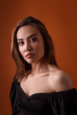 Turuncu arka planda koyu yakalı siyah elbise giyen zarif bir manken.