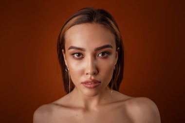 Akşam makyajlı, çıplak omuzlu, küpeli güzel Asyalı kız kameraya bakıyor.