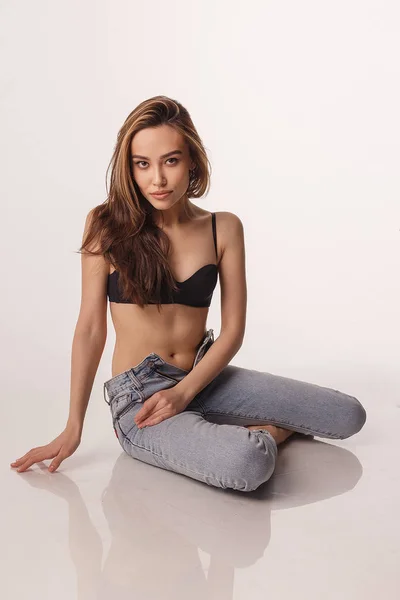 Sexy asiatische Frau posiert in schwarzen Dessous, blauen Jeans auf weißem Studiohintergrund — Stockfoto