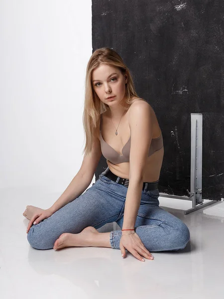 Sexy mulher caucasiana posando em lingerie bege, jeans azuis no chão do estúdio — Fotografia de Stock