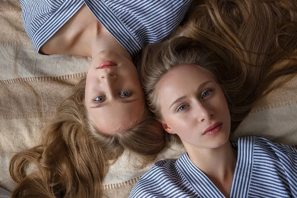 Duas jovens irmãs gêmeas muito caucasianas em camisas listradas oversize deitado no sofá — Fotografia de Stock