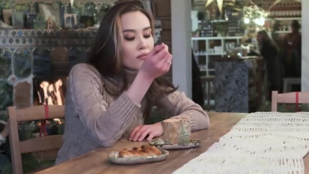 Cute young asian pretty girl sitting at cafe table, drinking coffee at fireplace — Stock Video