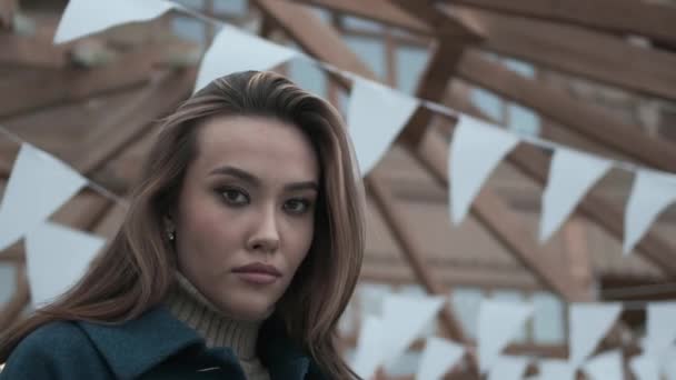 Fiatal ázsiai csinos lány kék kabátban, garbó hullámos haj néz kamera — Stock videók
