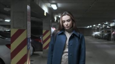 Paltolu şık düşünceli Asyalı kız yeraltı otoparkında yürüyor.
