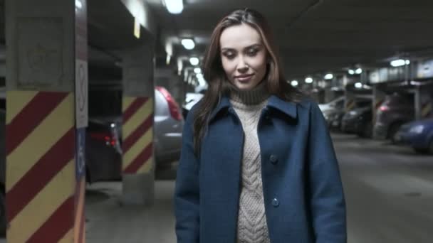 Stylish smiling cute asian girl in coat walks at underground parking along cars — 비디오