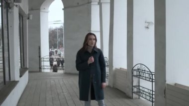 asian pretty girl in blue coat stands alone on veranda with white stone columns