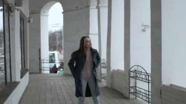 asian pretty girl in blue coat poses alone on veranda with white stone columns