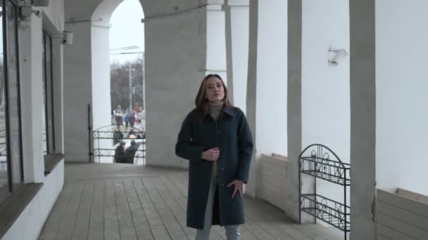 Asian pretty girl in blue coat walks forward on veranda with white stone columns — Stock video