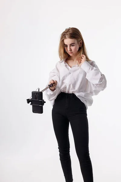 Молодая красивая девушка делает автопортрет со смартфоном, прикрепленным к селфи-палочке — стоковое фото