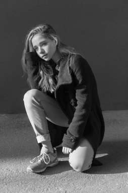 Uzun saçlı, kot pantolonlu, üzgün, yalnız bir genç kızın siyah beyaz portresi.