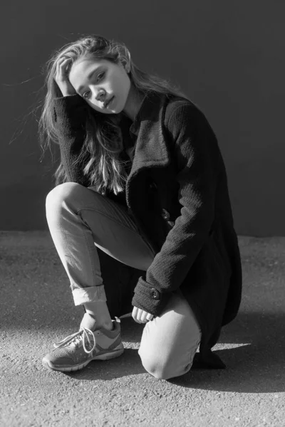 Черно-белый портрет грустной одинокой девушки с длинными волосами в пальто, джинсах — стоковое фото