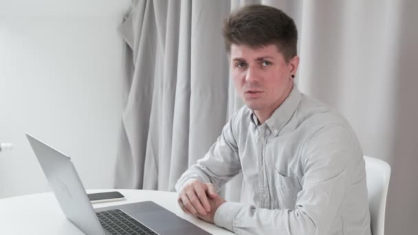 Hombre de negocios caucásico serio se sienta a la mesa con el ordenador portátil, teléfono inteligente, habla — Vídeos de Stock