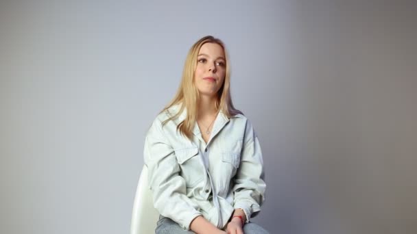 Pretty girl looking at camera in silence, sitting on chair on white background — Stock Video