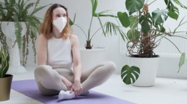Koruyucu maske takan genç kız lotus pozisyonunda oturur, güler ve meditasyona başlar.