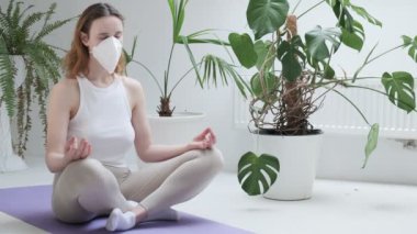 Koruyucu maske takan kız Lotus pozu verip meditasyon yapıyor. ev konsepti