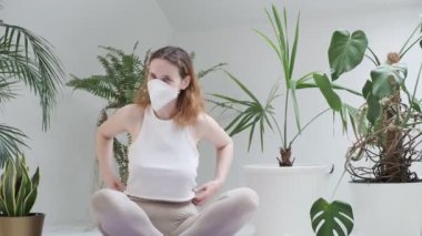 Koruyucu maske takan genç kız lotus pozisyonunda oturur, güler ve meditasyona başlar.