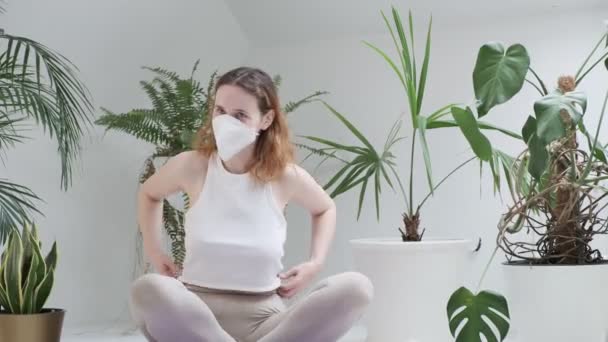 Молодая девушка в защитной маске сидит в позе лотоса, смеется, начинает медитацию — стоковое видео