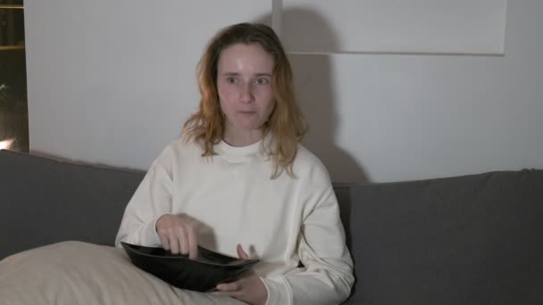 Девушка ест нездоровую пищу, смотрит телешоу поздно вечером. шокированное удивленное выражение лица — стоковое видео