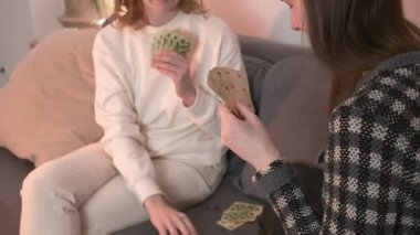 Arkadaşlar konuşur, evde poker oynar, eğlenir, güler. Kızlar kanepede kağıt oynar.
