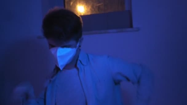 Ung man i skyddande medicinsk mask dansar nära fönstret. teal och orange scen — Stockvideo