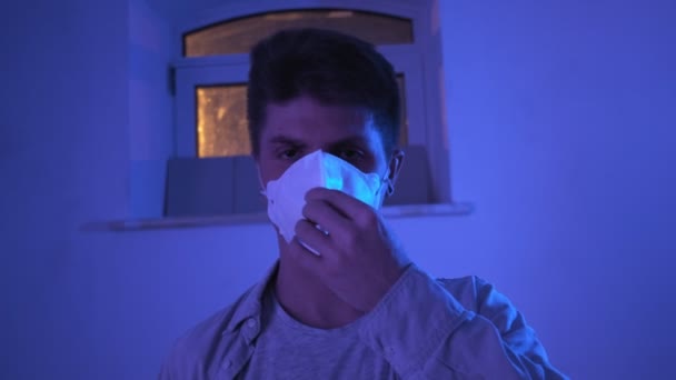 Brutal joven caucásico hombre pone en protector médico máscara en verde azulado, naranja luz — Vídeo de stock