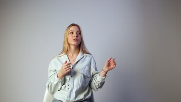Leende känslomässig flicka med blont långt hår berättar något i vit studio — Stockvideo