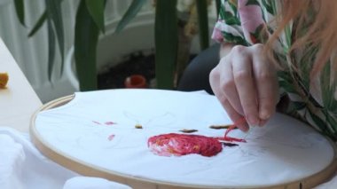 İğneyle dikiş diken kadın elleri. Nakışlı halka, renkli desenli kumaş.