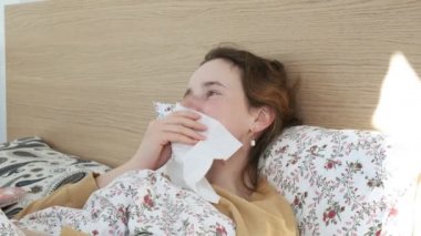 Hasta kız hapşırıyor, üflüyor, kağıt mendille burnunu siliyor. Kadın yatakta öksürüyor.