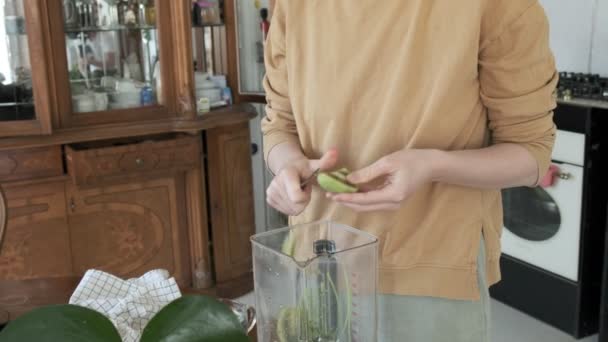 Flicka skär kiwi med kniv hemma kök. mixer på bordet. att göra smoothies — Stockvideo